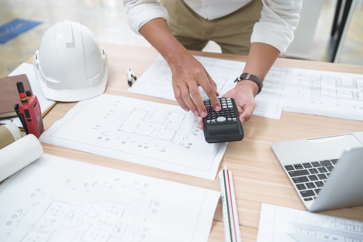 A construction professional analyzes architectural plans and uses a calculator for precise measurements and calculations, showcasing a typical work environment in the construction industry.