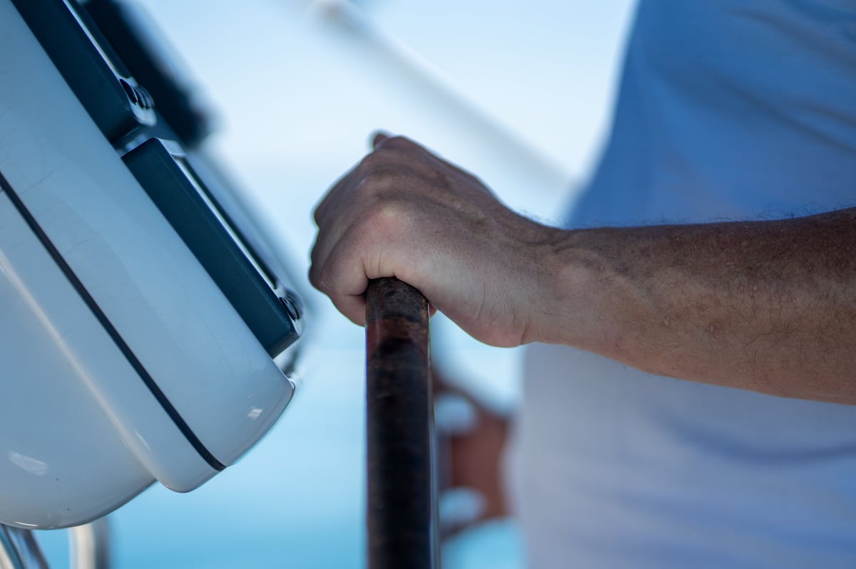 Person's hand gripping a ship's steering wheel for sailing and navigating
