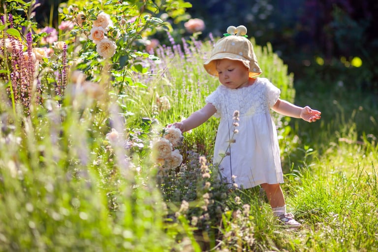 Happy toddler girl in a sun hat walking through a summer garden