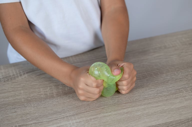 Close-up of child hands squeezing a translucent green sensory toy on a wooden table