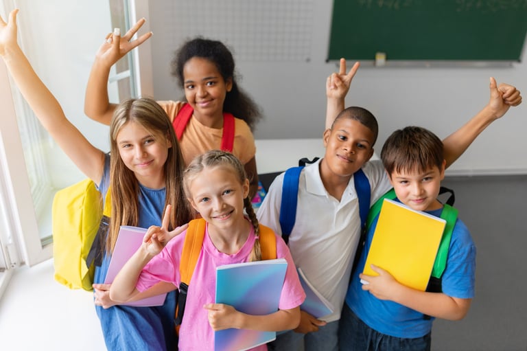 Cinco alumnos de primaria con mochilas y cuadernos sonriendo en un aula moderna