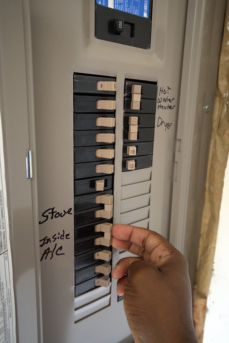 Hand turning on a flipped switch inside a residential electrical breaker box with labeled household circuits