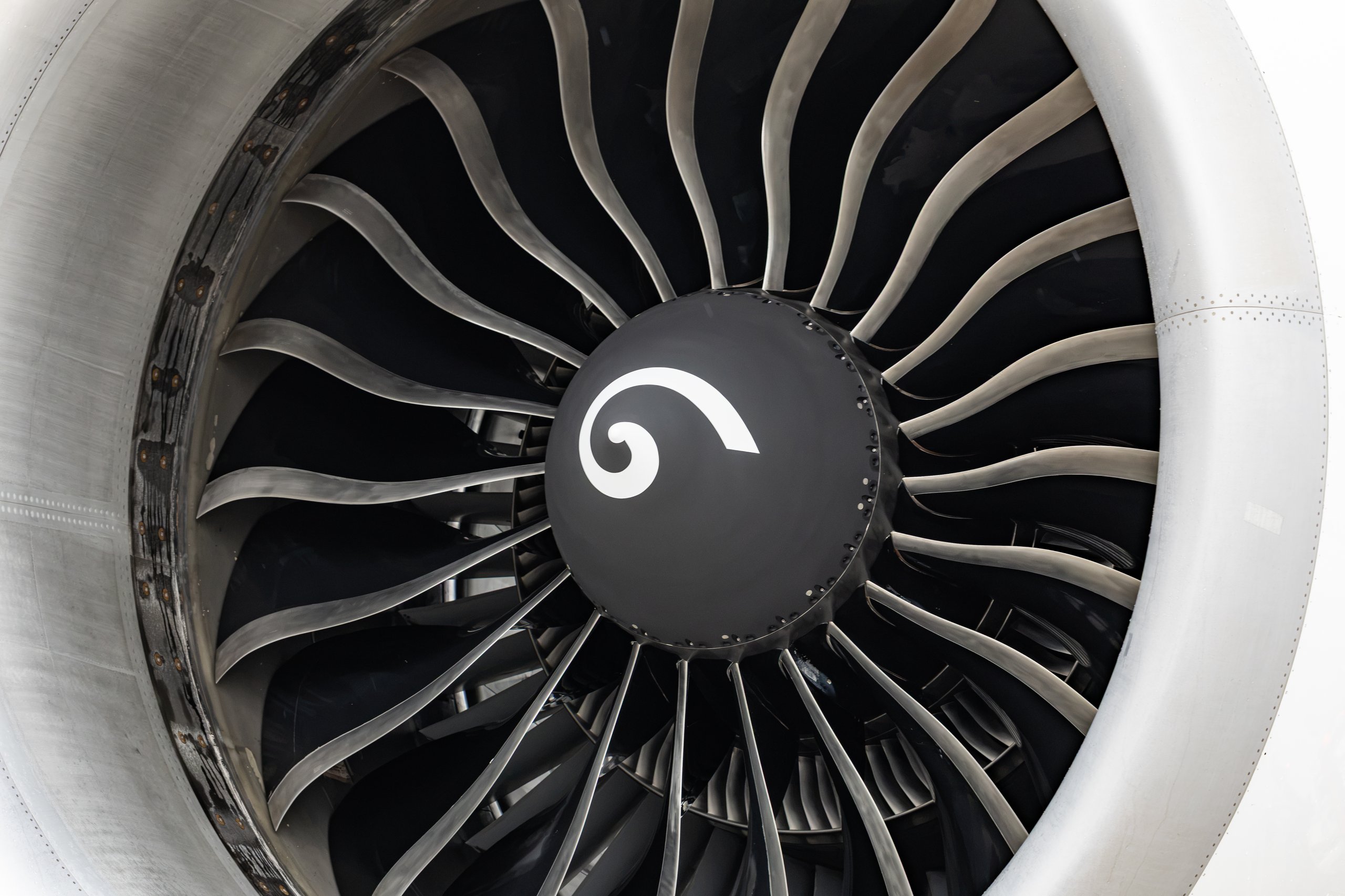 Close-up of a commercial airliner jet engine turbine fan blades with a white spiral on the black spinner hub