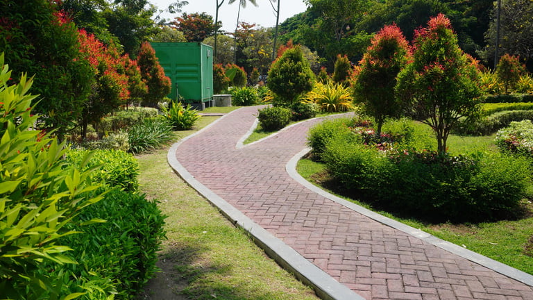 Forked red brick paved pathway winding through a lush garden in an urban park