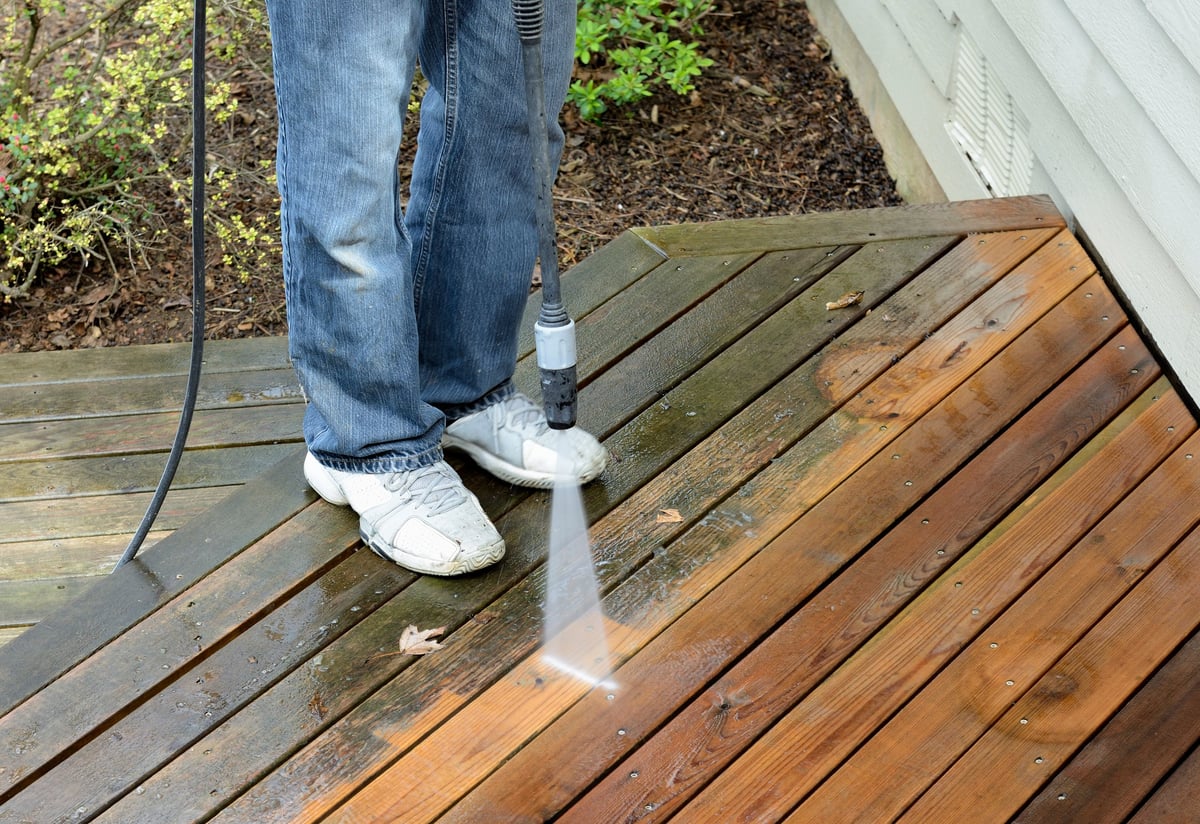 Contractor using a pressure washer to clean a cedar deck, deck restoration in progress
