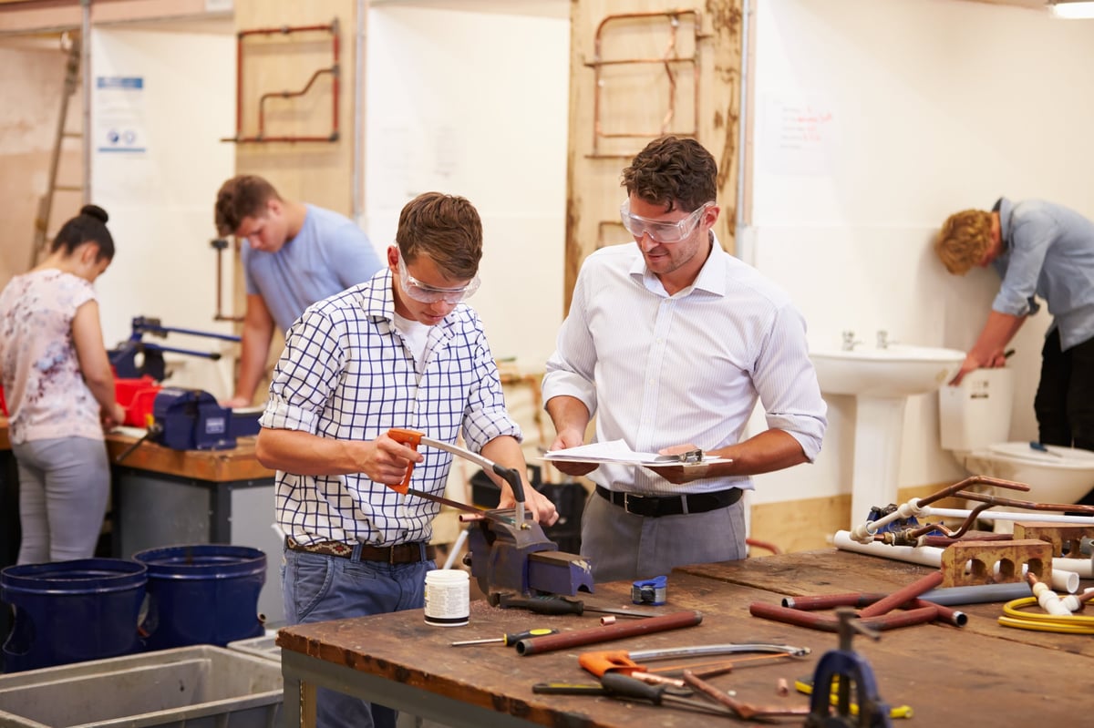 Students learning plumbing concepts and pipe work under qualified supervision with appropriate safety equipment