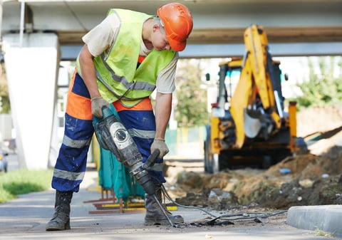 Worker with pneumatic hammer drill breaking asphalt at road construction