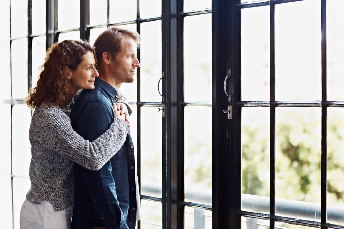 Zufriedenes Paar umarmt sich im neuen Zuhause am Fenster — Neuanfang nach einem stressfreien Umzug