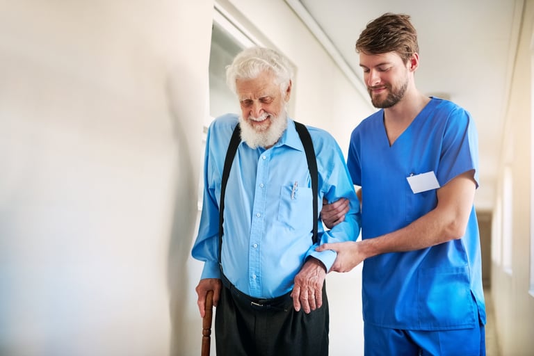 Mannelijke zorgprofessional die senior patiënt ondersteunt bij het lopen in de gang van een zorginstelling