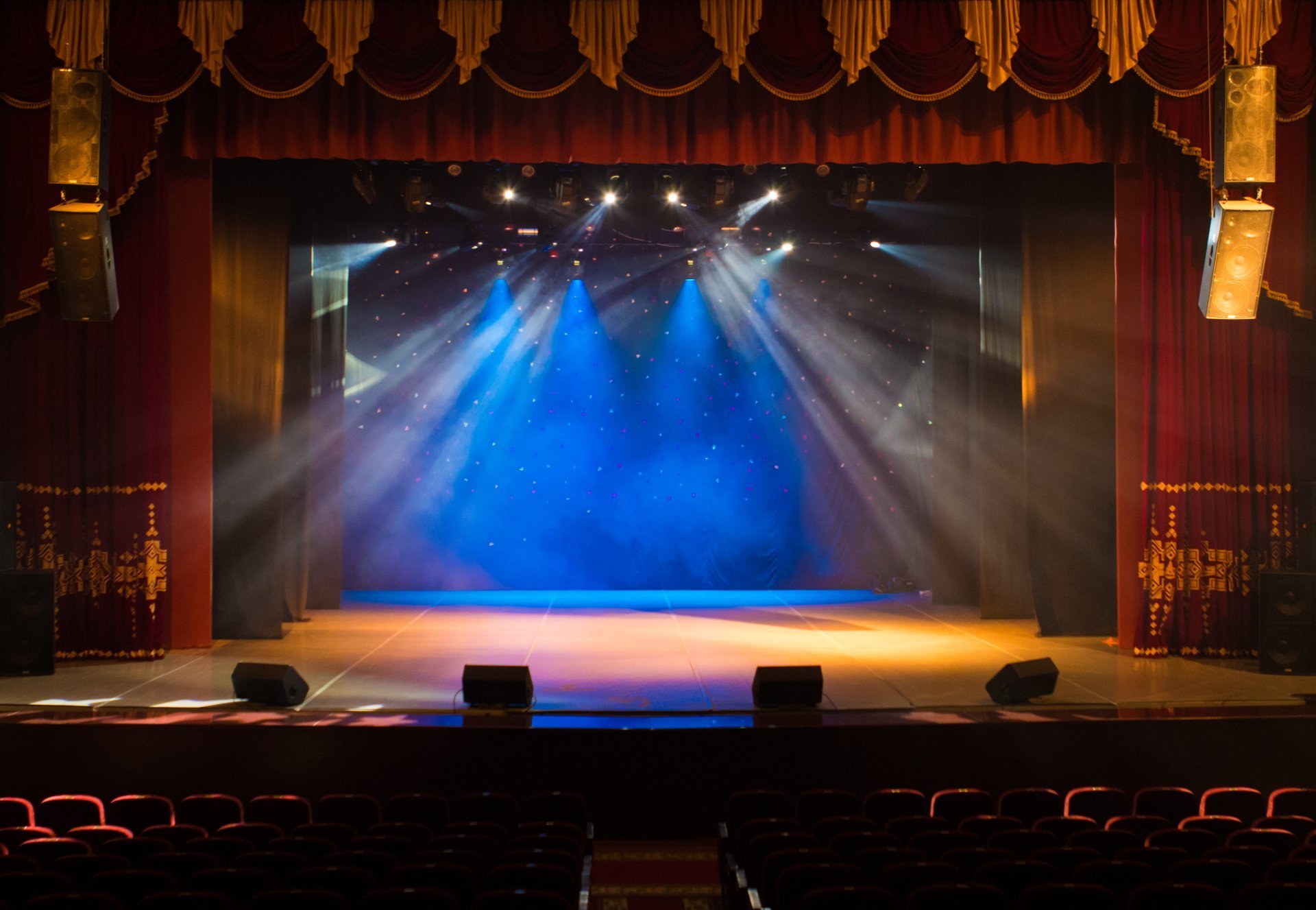 An empty theater stage lit by spotlights and haze