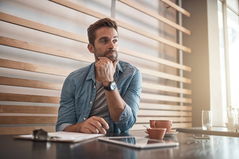 Handsome young man looking thoughtful while working in a coffee shop representing business decision making
