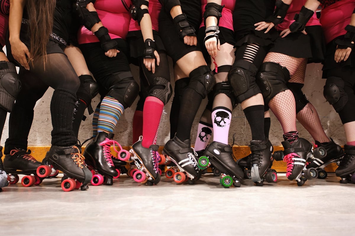 Roller derby team lined up showing legs wearing pink and black uniforms with colorful roller skates