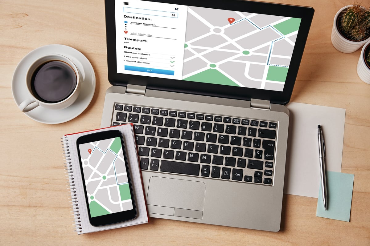 A GPS map navigation app open on a laptop and a smartphone on a wooden table