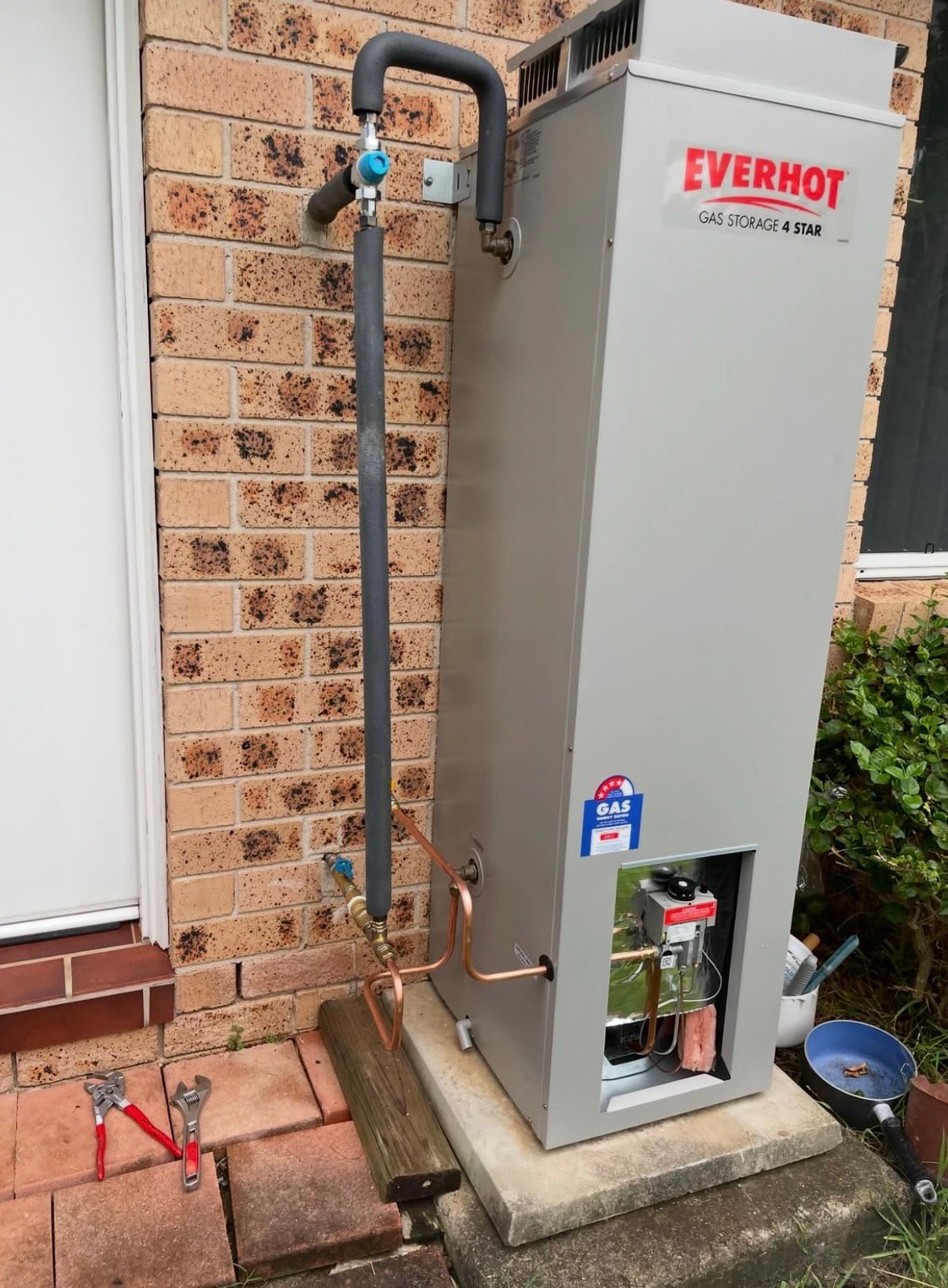 Everhot gas storage tank installed against brick wall with black pipe and blue valve connection