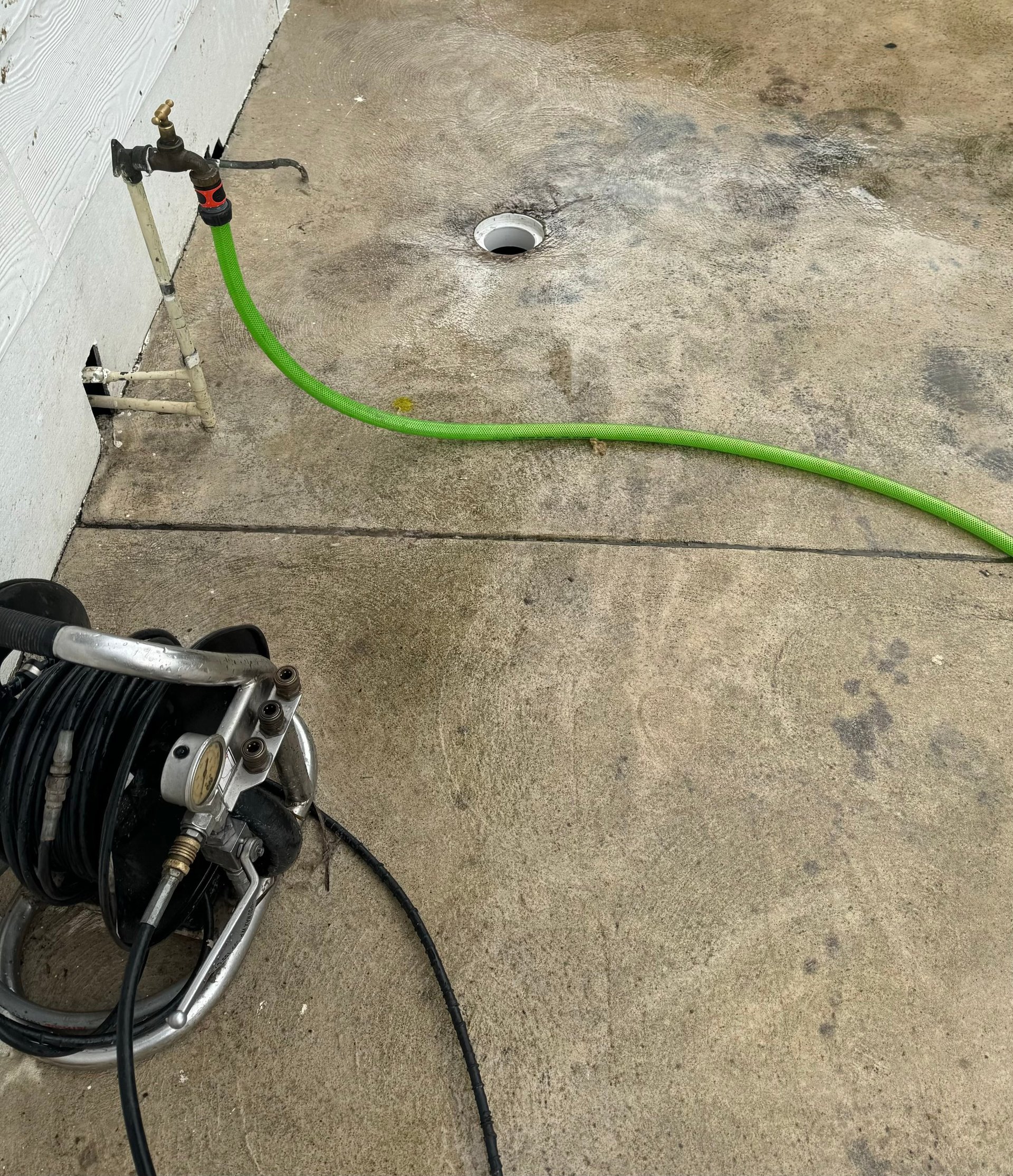 Overhead view of a green garden hose connected to a hose reel on a concrete driveway next to a white building