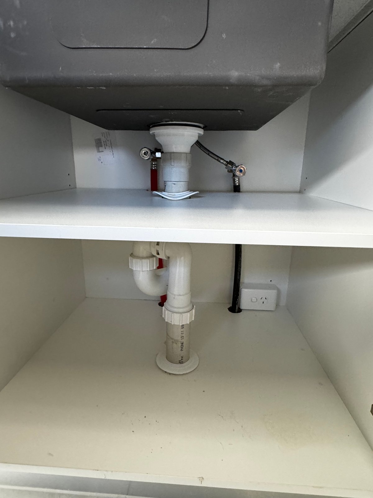 Interior view of bathroom sink cabinet showing drain pipes, p-trap, and water supply connections under the sink