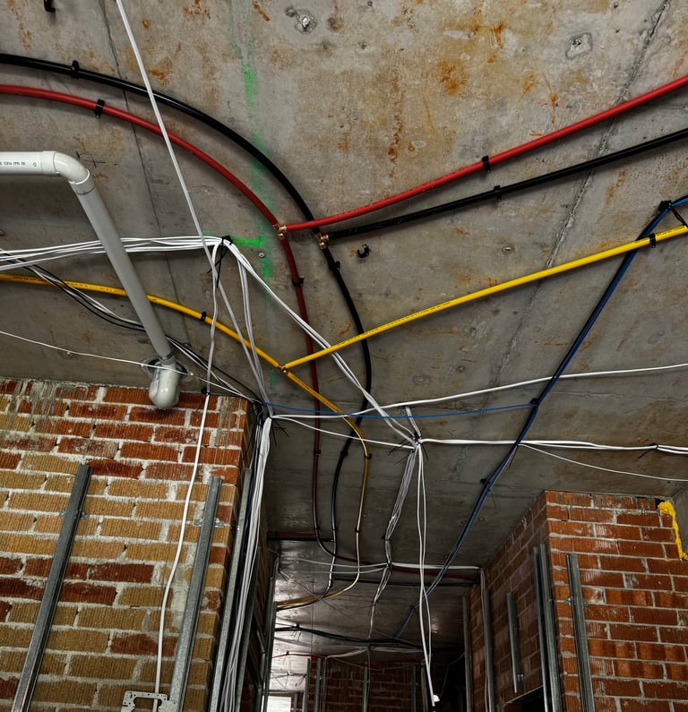 Electrical conduit and wiring in colored tubes mounted on concrete ceiling above brick wall frame