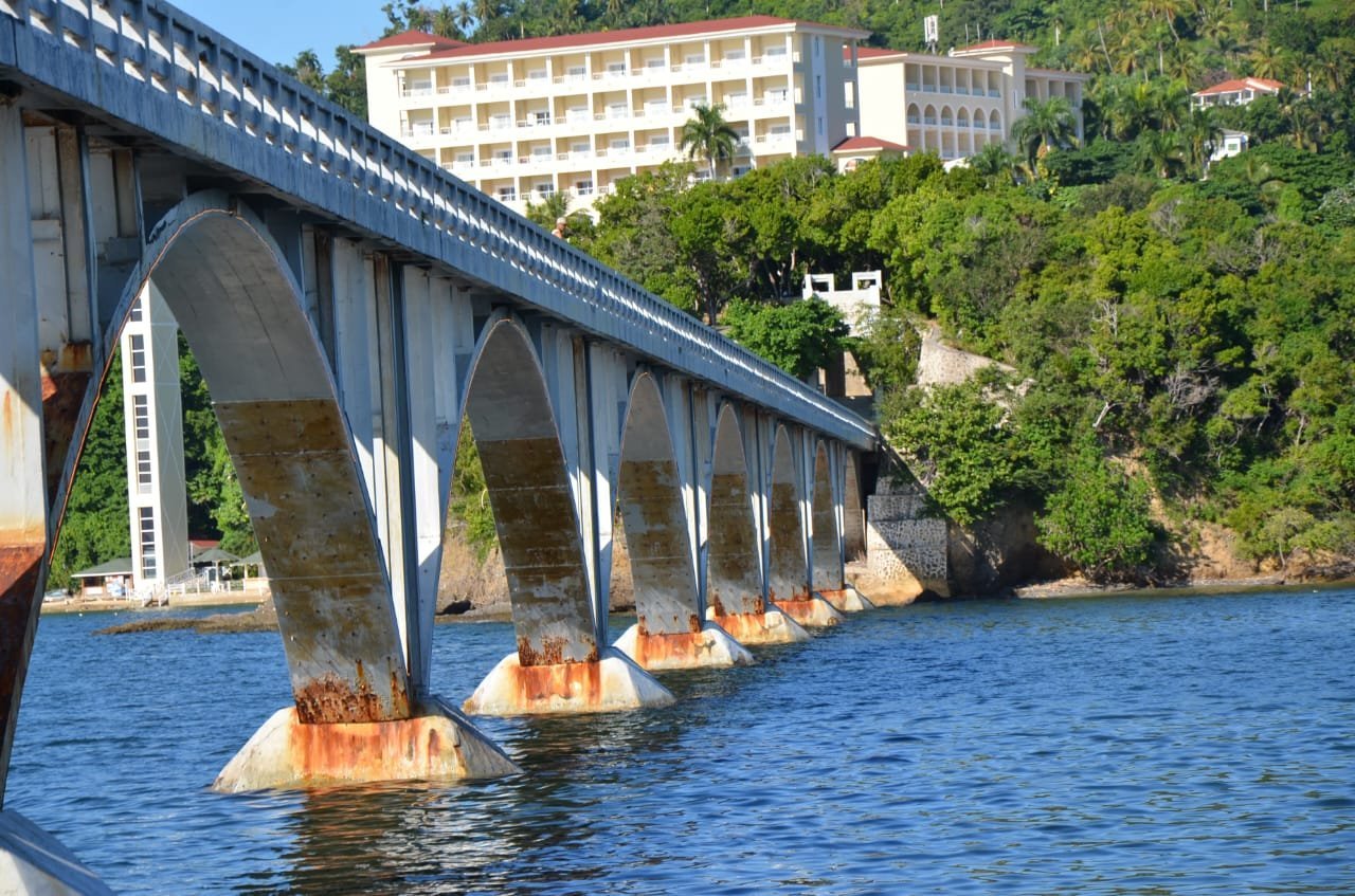 Gran puente arqueado sobre agua azul con edificios y colinas verdes de fondo