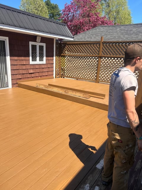 After: Man standing on large wooden deck of red cottage with lattice privacy screen and trees in background