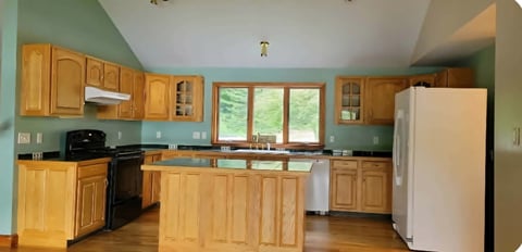 Before: Spacious kitchen with oak cabinets, green walls, large window, white refrigerator, black stove, and wooden island counter