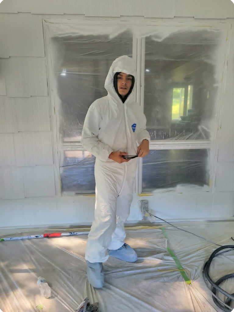 Person wearing white protective suit and hood standing in construction area with plastic sheeting and drywall