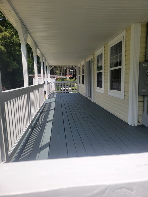 After: Long covered porch with dark gray composite decking, white railings, and white siding house exterior