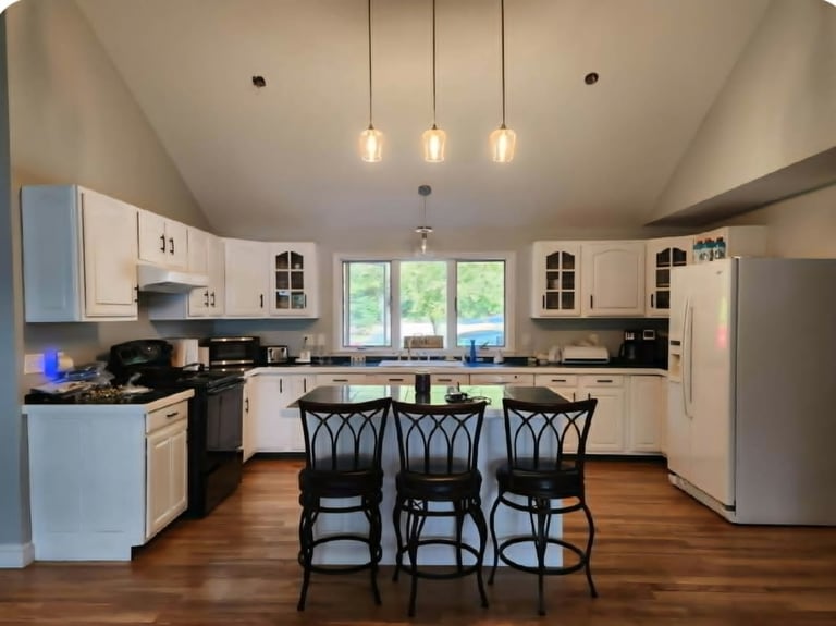 Modern kitchen with white cabinetry, stainless steel appliances, island with black chairs, and pendant lighting
