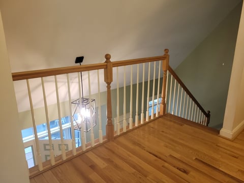 Before: Wood staircase landing with safety gate installed between wooden handrails, overlooking lower floor