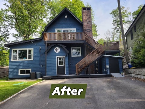 After: Dark blue two-story residential house with brick chimney and wooden deck, after renovation