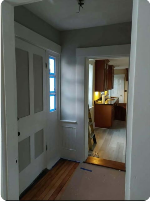 After: Entryway with white door, window with blue trim, and view into kitchen with dark wood cabinets and hardwood flooring