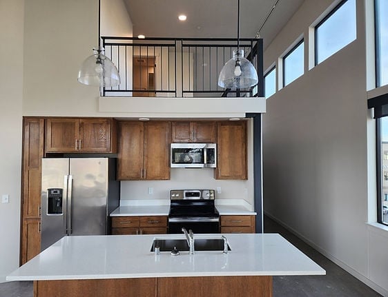 Modern kitchen with wood cabinets, white countertop island, stainless steel appliances, and upper loft area with railing