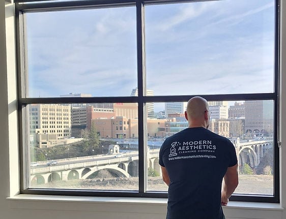 Person in black shirt looking out large window at city skyline with historic bridge and buildings below