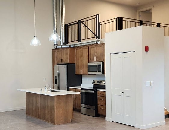 Modern kitchen with wood cabinetry, stainless steel appliances, island, and loft space above with metal railing