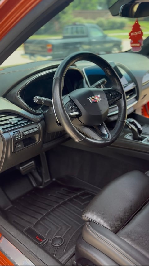 Cadillac interior showing steering wheel, dashboard, and front seats with a red air freshener hanging from the rearview mirror