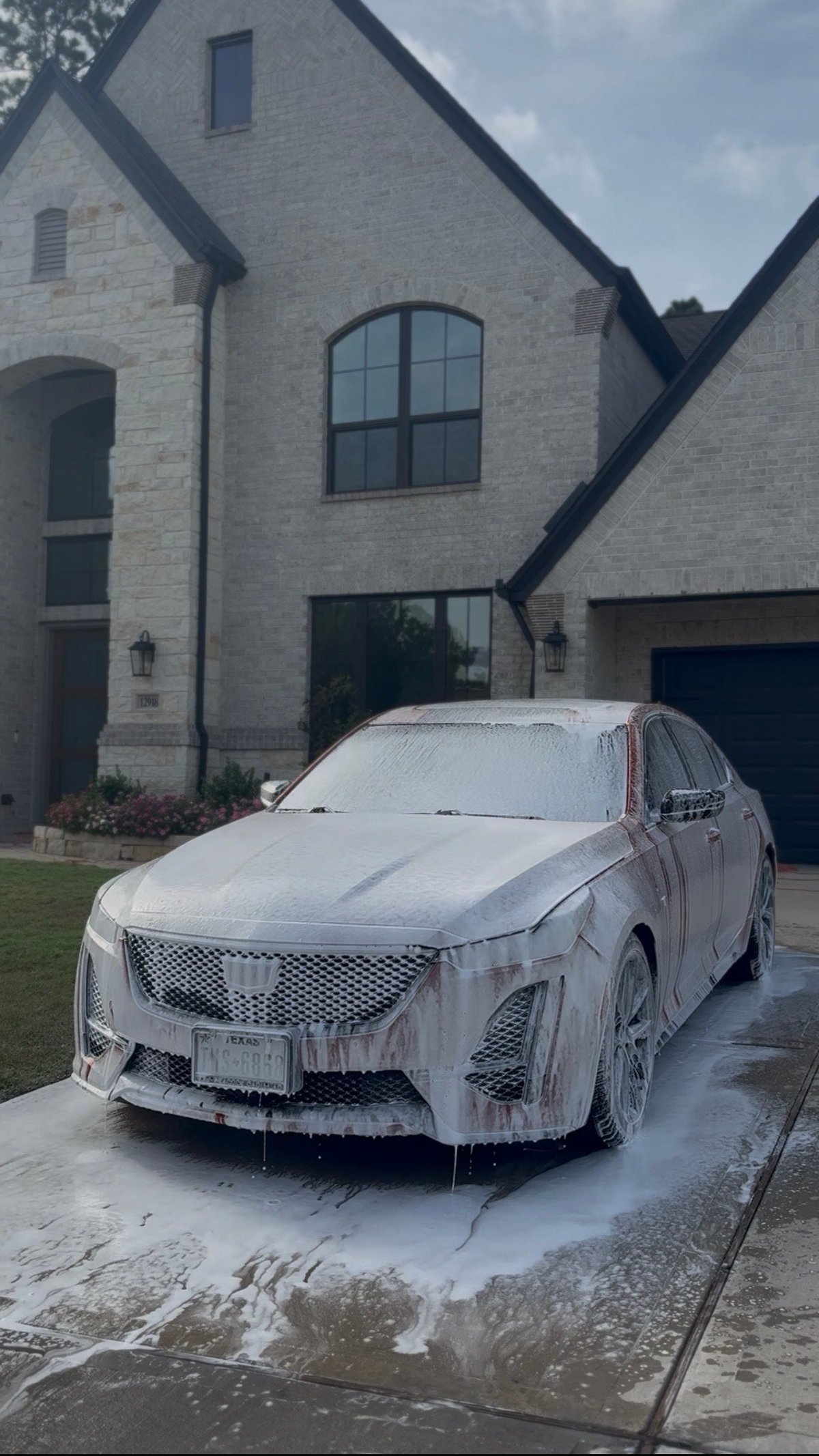 Orange Cadillac CT4 sedan covered in soap suds during a foam wash in a stone-house driveway — KJAJ Details before
