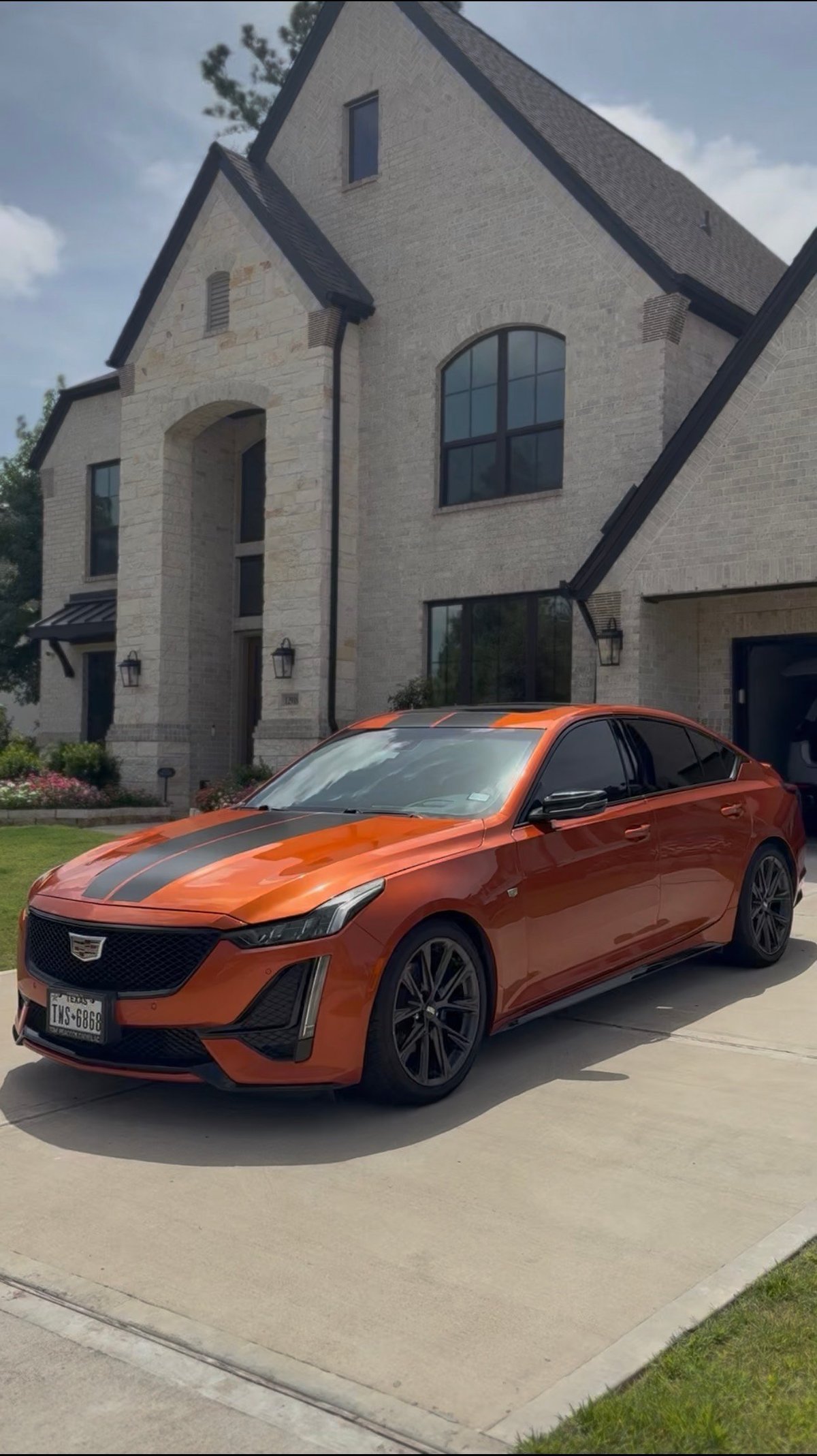 Orange Cadillac sedan with black racing stripes and deep gloss finish parked on a stone-house driveway — KJAJ Details after