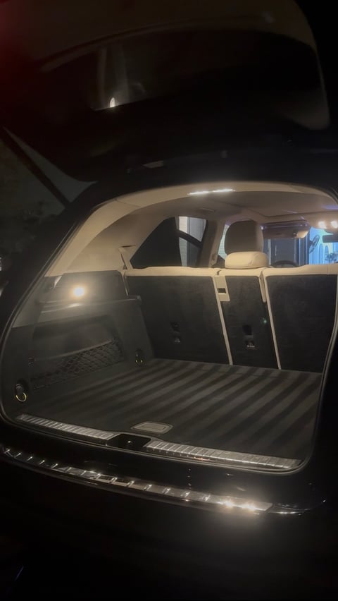 Open car trunk illuminated at night, showing empty cargo area with ribbed rubber mat and beige interior trim