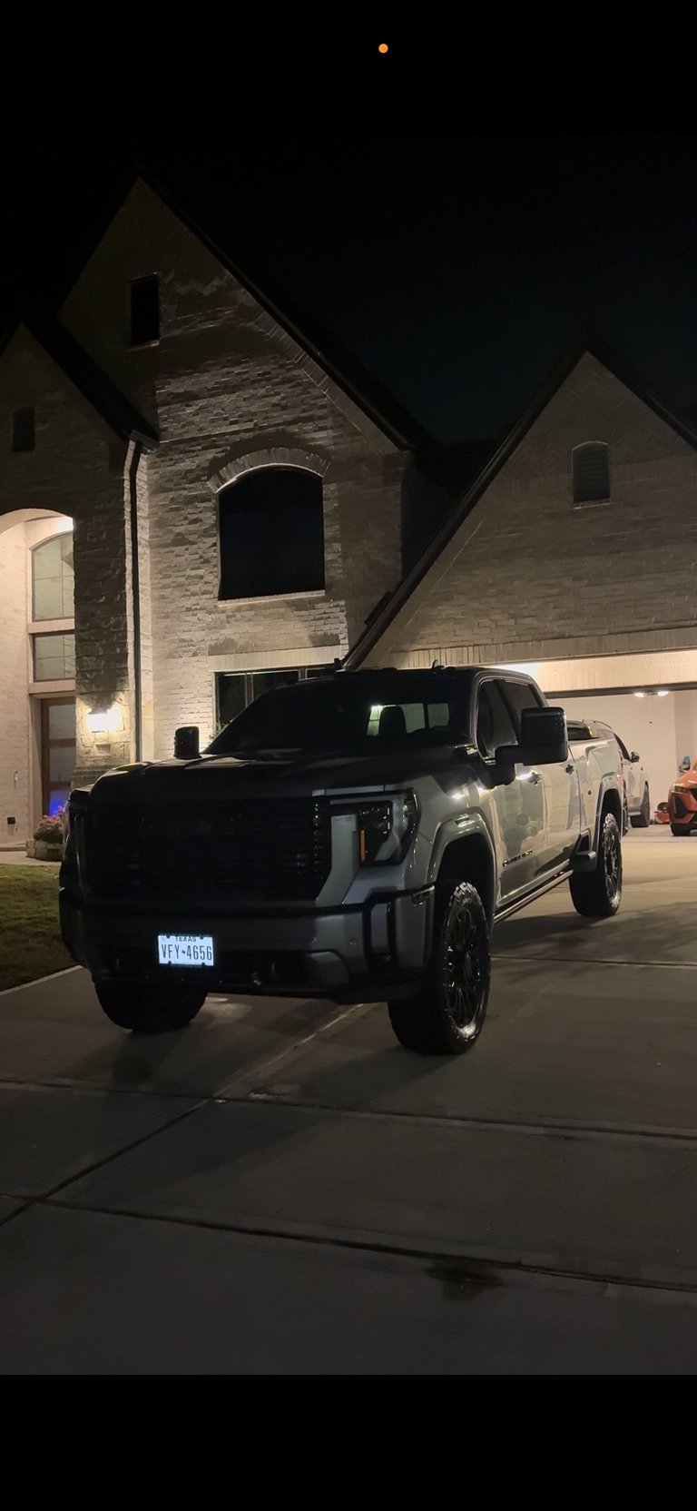 GMC pickup truck parked in a driveway at night in front of a modern stone house with illuminated exterior — KJAJ Details finished detail