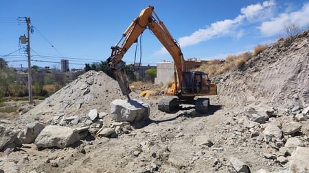 Orange excavator loading rocks and debris at a construction or mining site under clear blue sky