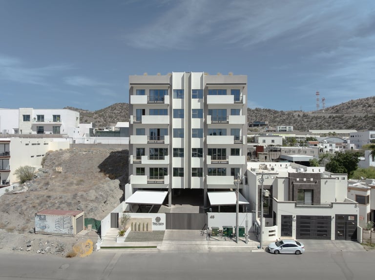 Modern white residential building with vertical ribbed design in arid hillside setting, parked vehicle visible at street level