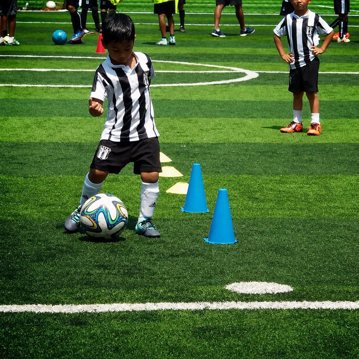 Young soccer player in striped jersey dribbling ball through blue cones during training on grass field