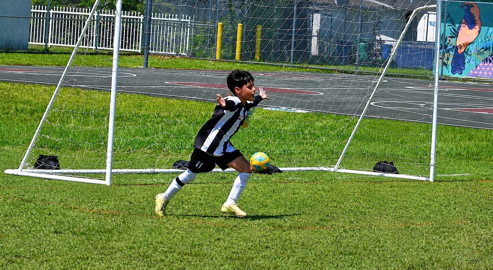 Young soccer player in black and white jersey kicking ball between white goal posts on grass field