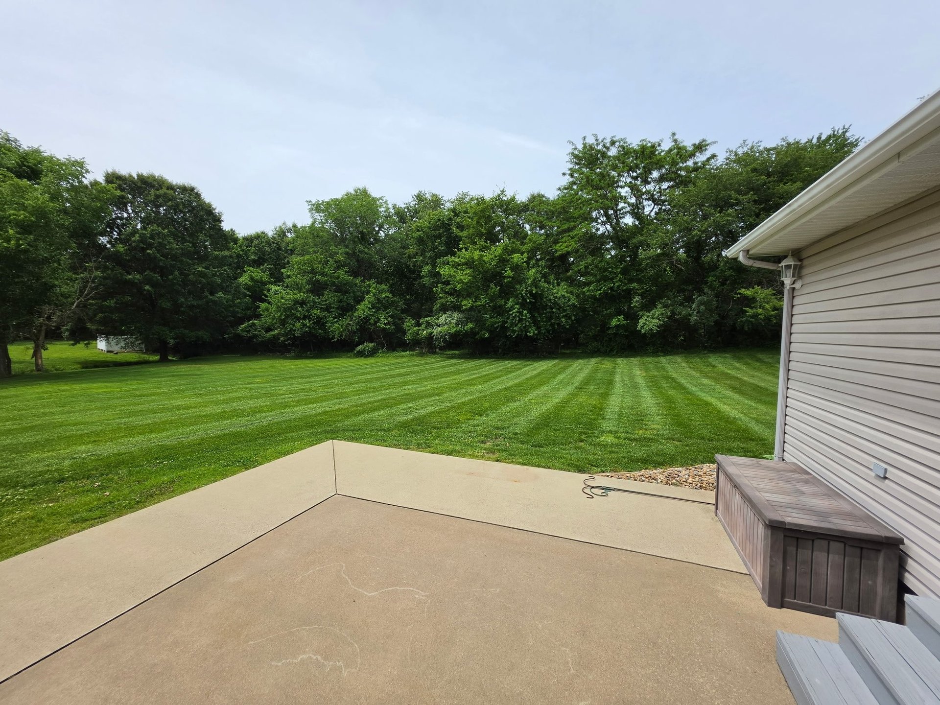 Concrete patio with lawn striping and trees in background, viewed from house edge