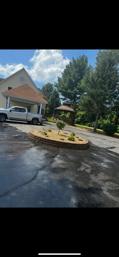Residential home with white truck parked in driveway, curved landscaped garden, gazebo, and tall trees under blue sky