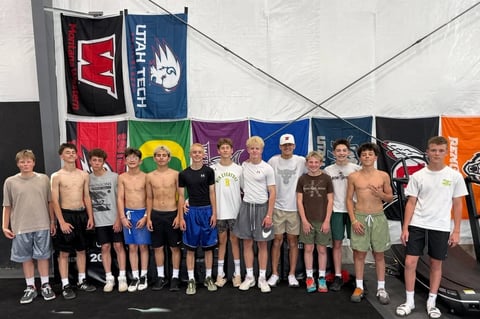 Group of young wrestlers posing together in front of colorful championship banners in a gymnasium