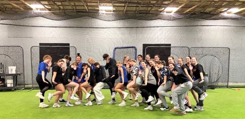 Group of athletes in blue and black athletic gear posing together on an indoor soccer field