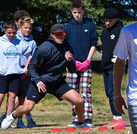 Outdoor wrestling or sports coaching session with instructors demonstrating technique to young students on grass field