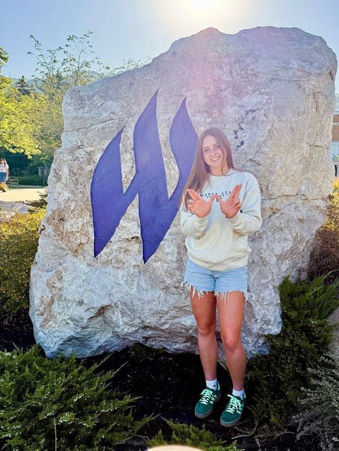 Young woman posing in front of a large stone monument with blue flame symbol, wearing casual clothing and sneakers