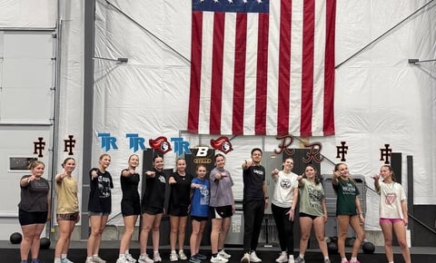 Group of young athletes posing together under an American flag in an indoor gymnasium