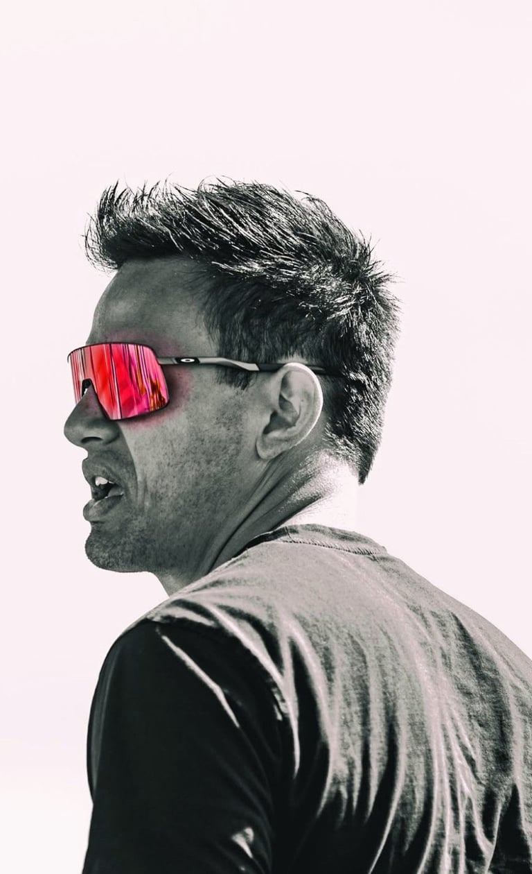 Man in profile wearing oversized red sunglasses and dark shirt against pale pink background
